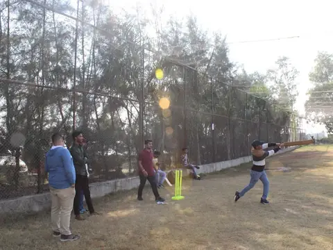 Team members playing cricket on an outdoor ground during a team outing
