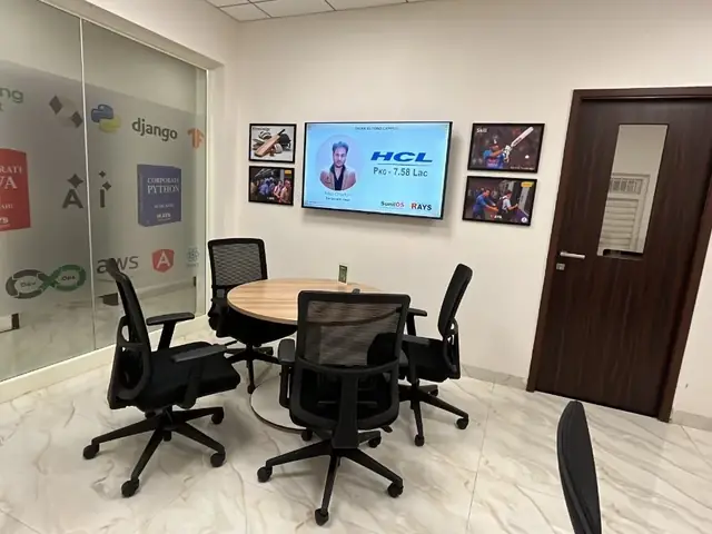 Small discussion room at Rays EdTech with a round table and a wall-mounted screen showing a placement announcement